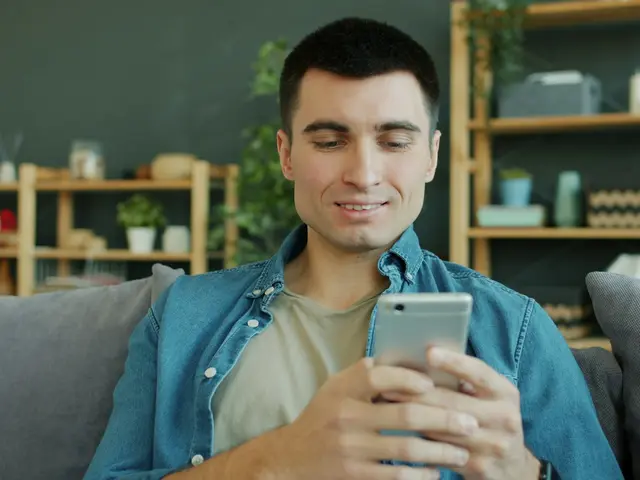 A man relaxing on his sofa, smiling at his phone