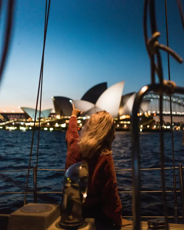 A woman on a boat in Sydney Harbour pointing at the Opera House